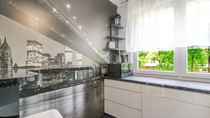 Une cuisine ornée d’une fresque représentant un paysage urbain, équipée d’un four à micro-ondes et dotée d’une fenêtre donnant sur un espace verdoyant.