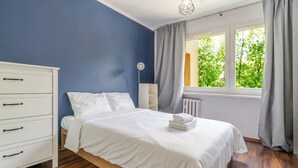 Une chambre à coucher avec un lit, une commode, une fenêtre avec des rideaux et un radiateur.
