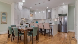 Una cocina moderna con armarios blancos, una isla central con sillas, un refrigerador de acero inoxidable e iluminación colgante.
