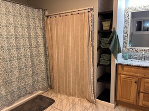 Ein Badezimmer mit gemustertem Duschvorhang, einem Holzkabinet und einem gefliesten Boden.