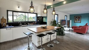 A modern kitchen with a central island, bar stools, pendant lighting, and a red sofa in a living area. - Gorgeous home in Leon (Leon)