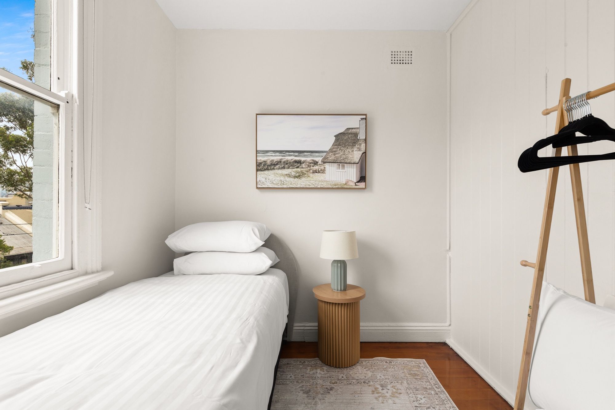 Une chambre à coucher avec un lit, des oreillers, une lampe, un tableau et un porte-manteau.