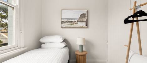 Une chambre à coucher avec un lit, des oreillers, une lampe, un tableau et un porte-manteau.