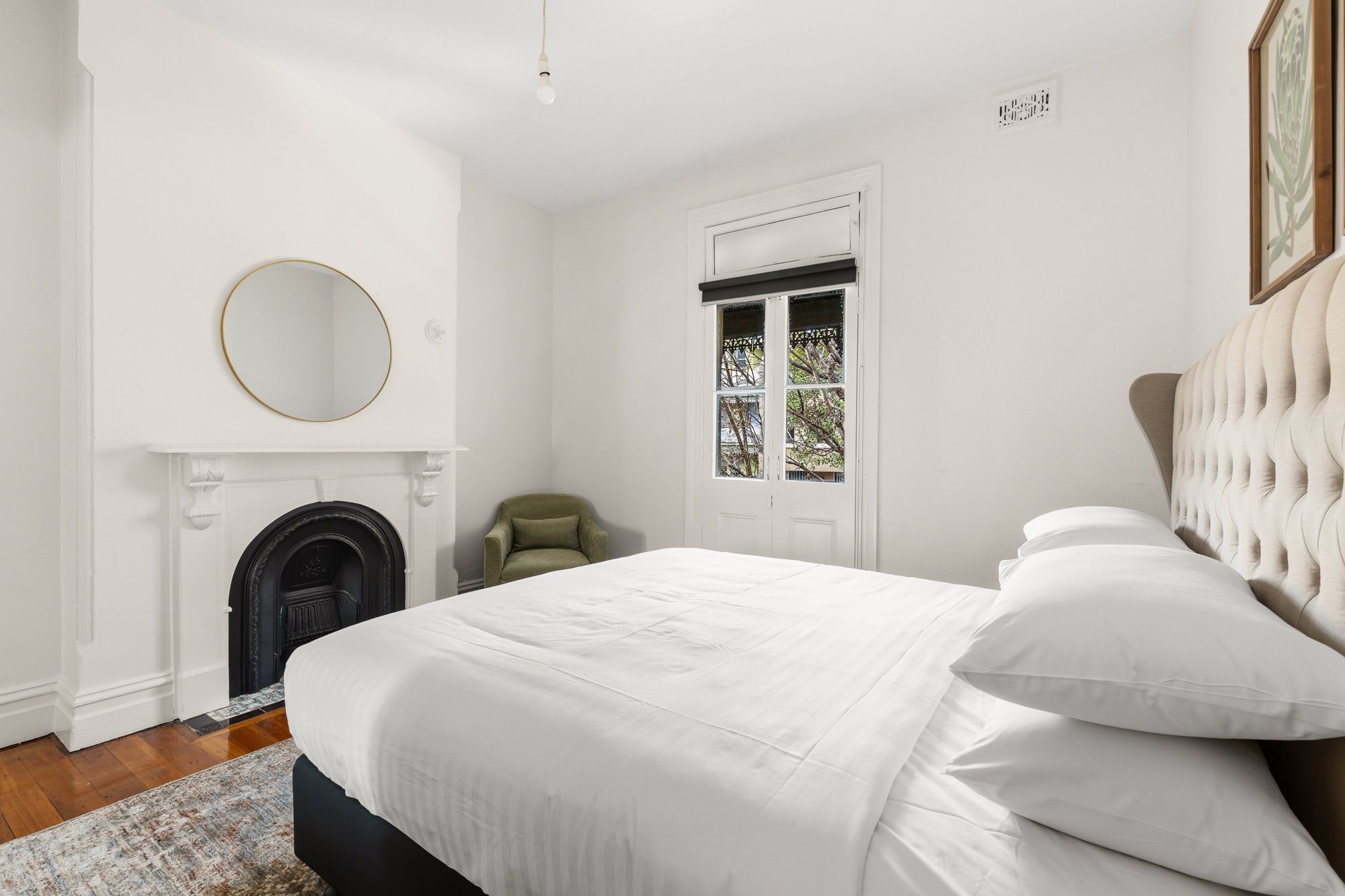 Een slaapkamer met een bed, een ronde spiegel, een open haard en een raam met uitzicht.