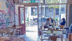 Un café interior con mesas y sillas, una barra con productos y vistas a la calle.