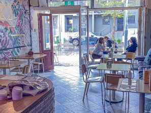 Ein gemütliches Café mit Tischen, Stühlen und einer Theke mit Waren, mit Blick auf die Straße.
