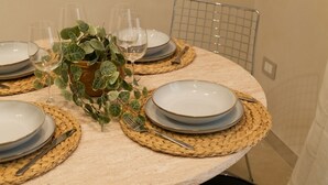 Et rundt spisebord dækket med tallerkener, glas og bestik, omgivet af vævede bordskåner og en potteplante.
