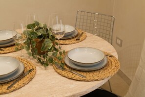 Ein runder Esstisch ist gedeckt mit Tellern, Gläsern und Besteck, umgeben von gewebten Tischsets und einem Blumentopf.
