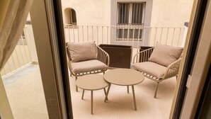 En balkon med to stole og et lille bord, et vindue med tremmer og en dørkarm.