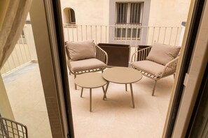 Ein Balkon mit zwei Stühlen und einem kleinen Tisch, ein Fenster mit Gittern und ein Türrahmen.