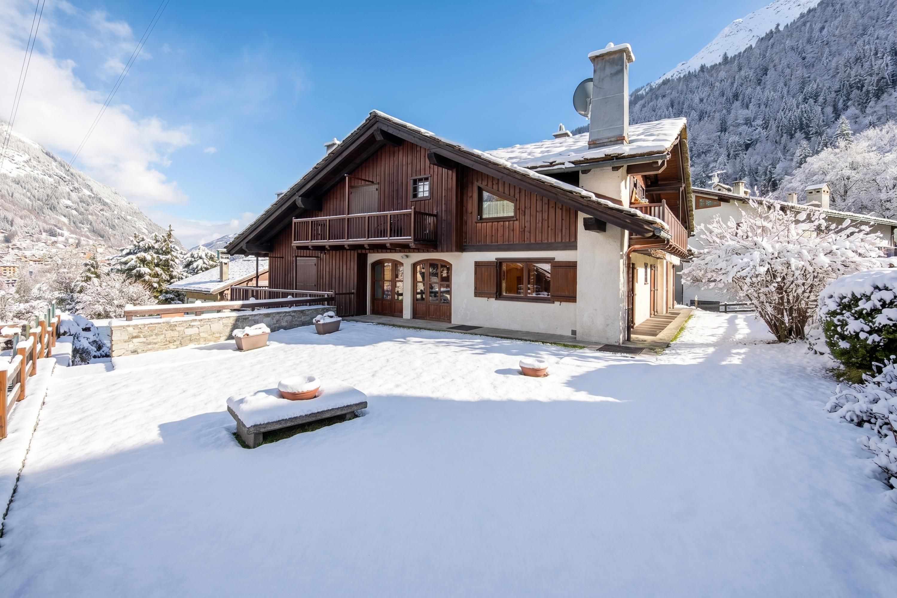 A wooden chalet with a balcony, set in a snowy mountainous area.