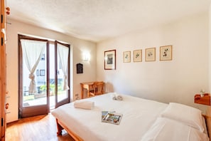 A hotel room with a bed, a wooden desk, a chair, a door with curtains, and a wall with framed pictures. - Family Apartment Steps From Ski Lifts, Courmayeur, Italy (Courmayeur)
