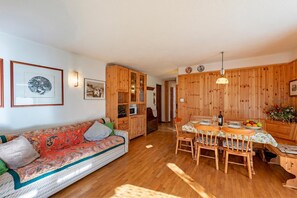 A cozy room with a sofa, wooden cabinets, a dining table with chairs, and a kitchen area. - Family Apartment Steps From Ski Lifts, Courmayeur, Italy (Courmayeur)