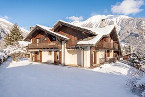 Ein Chalet mit Holzfassade, einem Balkon und einem mit Schnee bedeckten Dach, umgeben von Bergen.