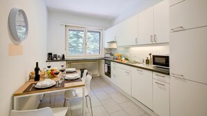 A modern kitchen with white cabinets, a dining table set for two, and a window providing natural light. - 76 The Lake House Sole, Melide, Switzerland (Melide)