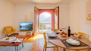 A modern living room with a TV, dining table, yellow chairs, and a balcony with a mountain view. - 76 The Lake House Sole, Melide, Switzerland (Melide)