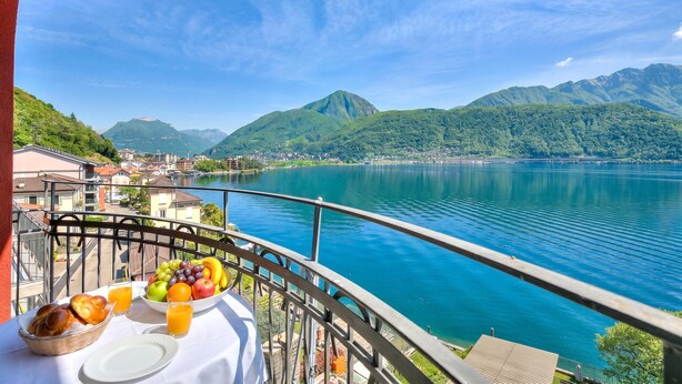 A balcony with a table set for breakfast, overlooking a lake and mountains. - 76 The Lake House Sole, Melide, Switzerland (Melide)