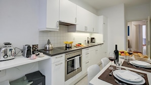 Eine moderne Küche mit weißen Schränken, einem Edelstahlbackofen und einer Frühstücksecke mit Obst und Brot.