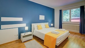 Ein Schlafzimmer mit Bett, Nachttischen, einem Fenster mit Vorhängen, einem Heizkörper und einer blauen Akzentwand.