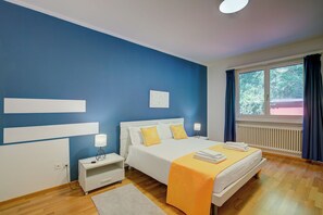 A bedroom with a bed, bedside tables, a window with curtains, a radiator, and a wall with a blue accent. - 76 The Lake House Saturno, Melide, Switzerland (Melide)