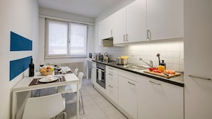Eine moderne Küche mit weißen Schränken, einem Esstisch mit Stühlen und einem Fenster mit Jalousien.