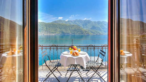Ein Balkon mit Frühstückstisch, mit Blick auf einen See und Berge.