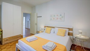 Hotellihuone, jossa on sänky, vaatekaappi, yöpöytä lampun kanssa ja pieni pyöreä pöytä lampun kanssa.