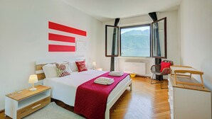 Un dormitorio con cama, mesitas de noche, un espejo, una ventana con vistas y una silla.