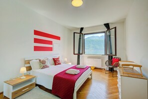 Ein Schlafzimmer mit Bett, Nachttischen, einem Spiegel, einem Fenster mit Aussicht und einem Sessel.