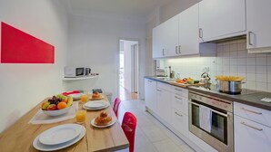Una cocina moderna con armarios blancos, una mesa de comedor con platos, un cuenco de fruta y una silla roja.