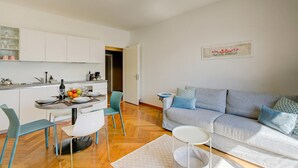 Un salon moderne avec un canapé gris, une table à manger avec des chaises et un coin cuisine doté de meubles blancs.