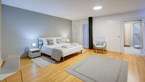 Une chambre moderne comprenant un lit, des tables de chevet, une chaise, un espace douche et une porte donnant sur une autre pièce.