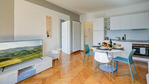 Une cuisine moderne avec des meubles blancs, une table à manger avec des chaises et un téléviseur à écran plat posé sur un meuble.