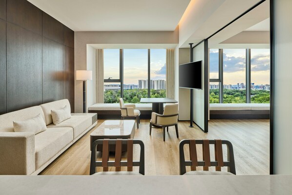 A modern hotel room with a sofa, chairs, a table, a TV, and large windows offering a city view. - Doubletree by Hilton Changsha Tianxin (Changsha)