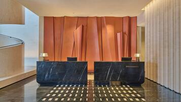 Zona de recepción con dos mostradores de mármol negro, piso estampado y una pared con paneles verticales.