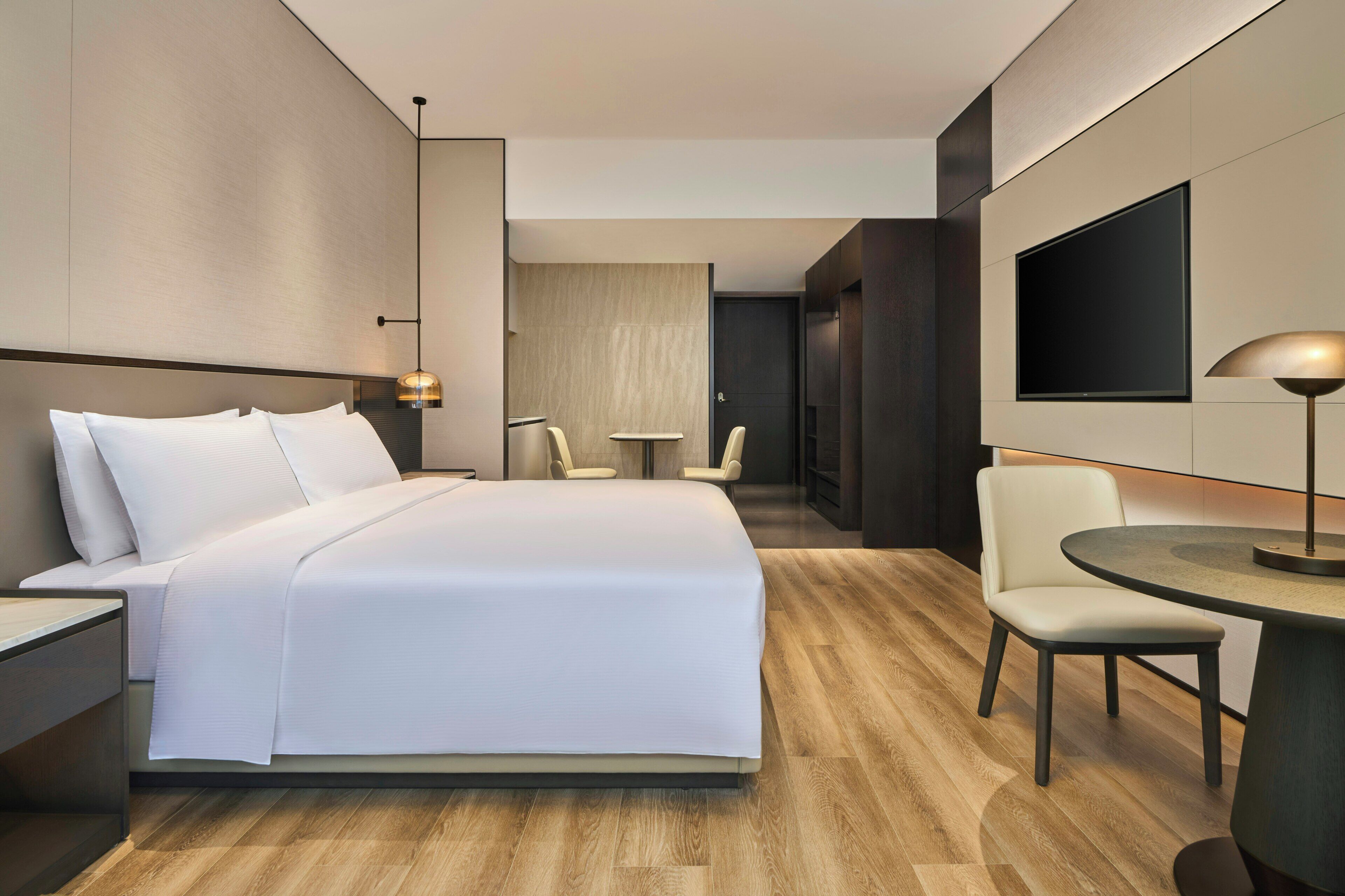 Une chambre d’hôtel moderne avec un grand lit, une table ronde et un téléviseur fixé au mur.