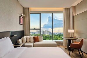 A hotel room with a bed, a sofa, a small table with a lamp, and a view of a cityscape through large windows. - Doubletree by Hilton Changsha Tianxin (Changsha)