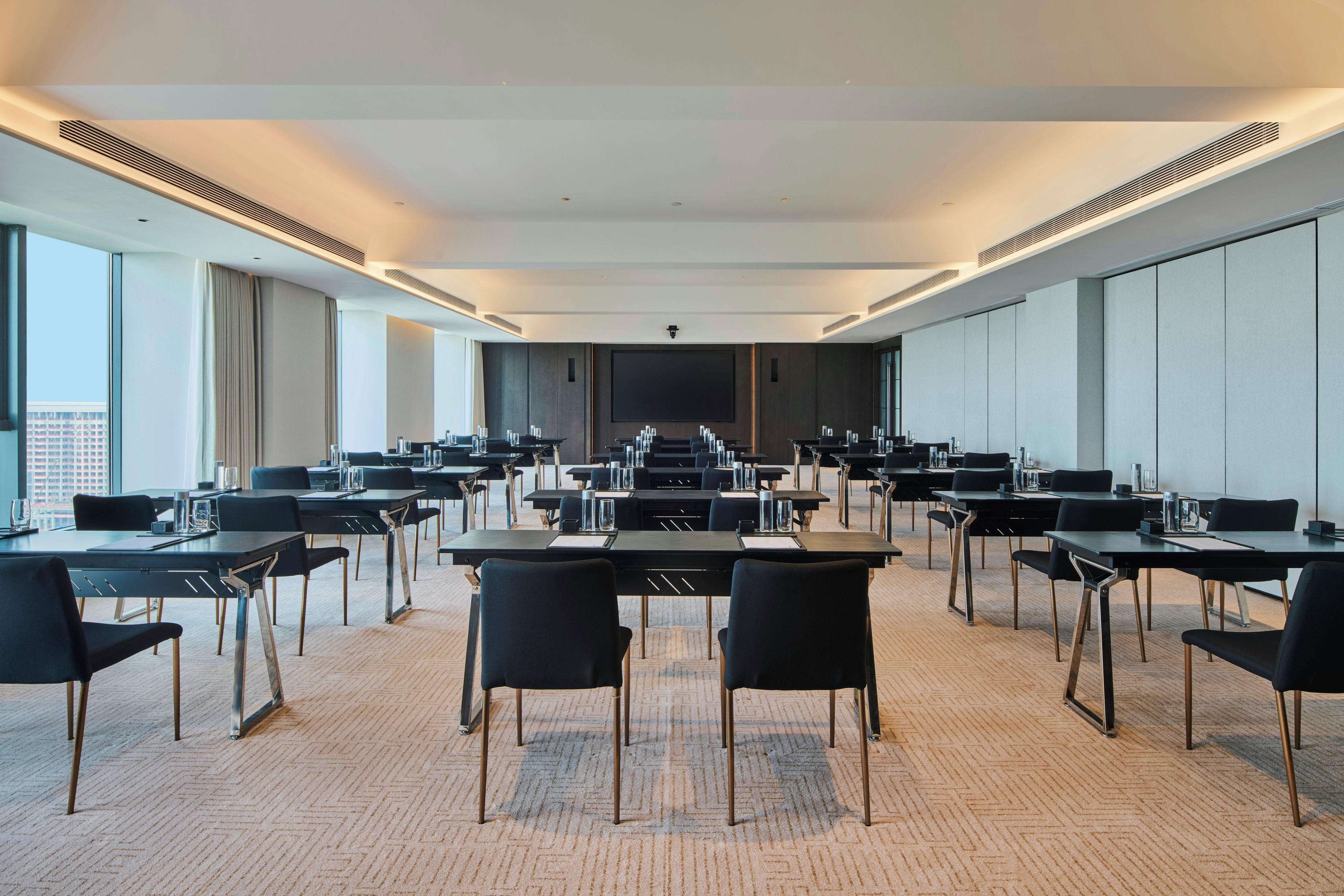 Un salón de conferencias con varias mesas y sillas, amplios ventanales y un techo alto.