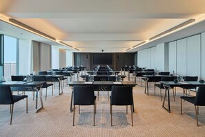 Un salón de conferencias con varias mesas y sillas, amplios ventanales y un techo alto.