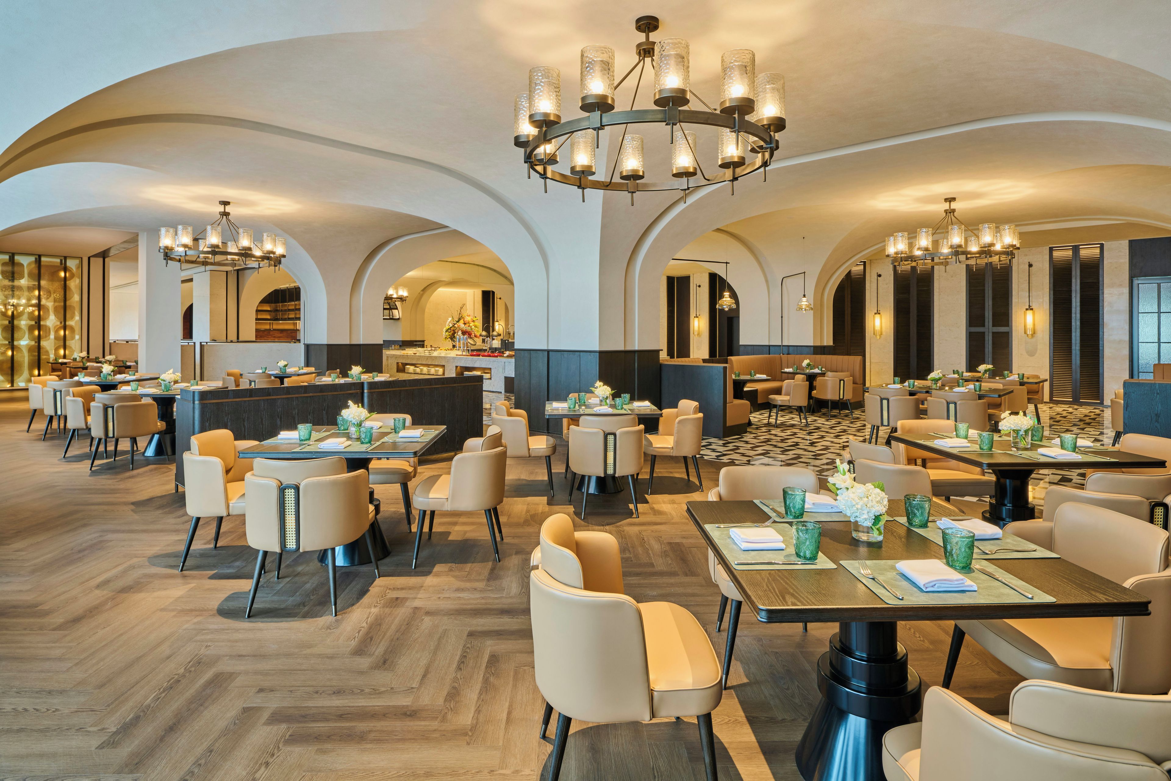Un comedor amplio con varias mesas y sillas, una barra central y un techo alto con candelabros.