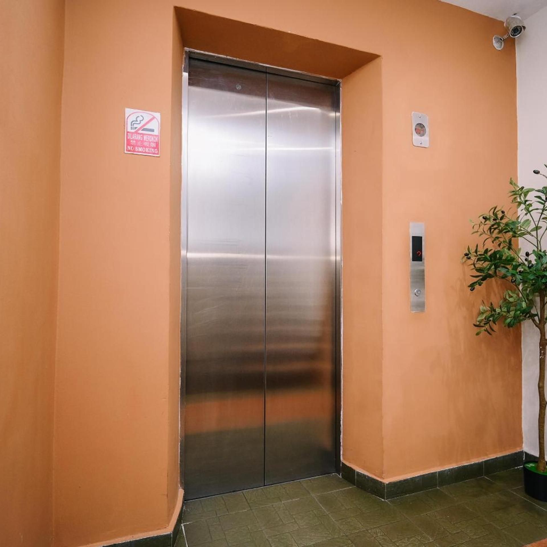 A metallic elevator door in a hallway with a 'No Smoking' sign and a potted plant.