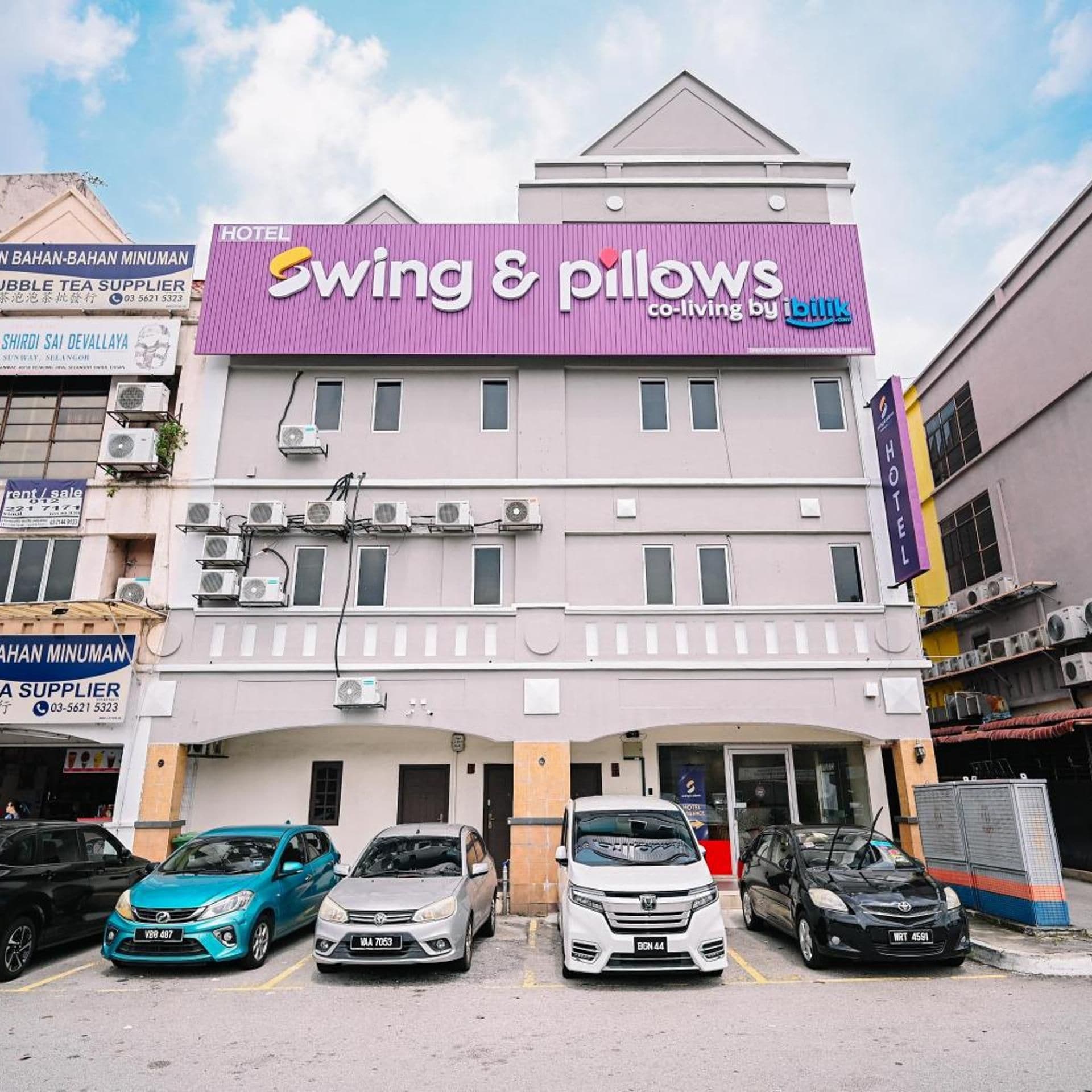 A hotel with a prominent sign for 'Swing & Pillows' and multiple parked cars in front.