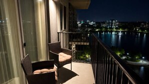 Ein Balkon mit zwei Korbstühlen, Blick auf eine nächtliche Skyline und ein Gewässer.