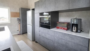 A modern kitchen with grey cabinetry, a built-in oven, a coffee maker, and a window providing natural light. - GREY HOUSE NISEKO (Niseko)