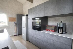 Eine moderne Küche mit grauen Schränken, einem eingebauten Backofen, einer Kaffeemaschine und einem Fenster, das natürliches Licht hereinlässt.