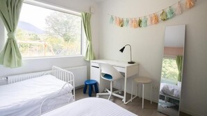 A bedroom with a bed, a desk, a chair, a radiator, and a window with curtains. - GREY HOUSE NISEKO (Niseko)