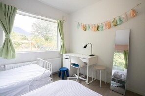 Ein Schlafzimmer mit Bett, Schreibtisch, Stuhl, Heizkörper und einem Fenster mit Vorhängen.