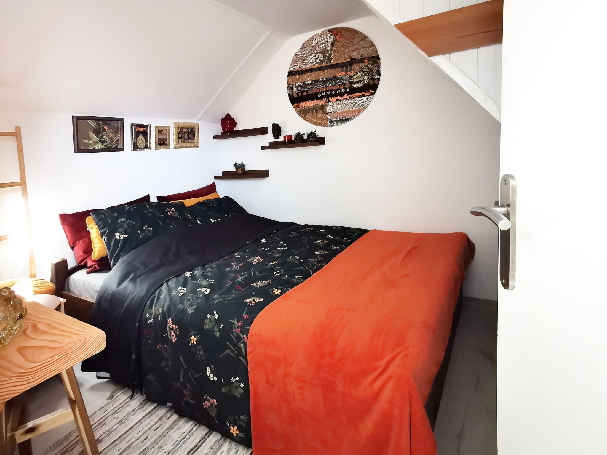 Ein Schlafzimmer mit einem Bett, einem Schreibtisch, einem Sessel, einem an der Wand befestigten Regal mit Dekorationen und einem runden Kunstwerk.