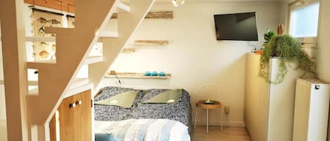 A compact bedroom with a bed, a small stool, a TV, and a radiator.