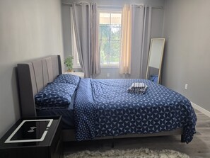 Ein Schlafzimmer mit einem Bett, Nachttischen, einem Spiegel und einem Fenster mit Vorhängen.